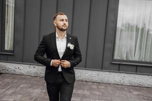 stylish and elegant groom in a black suit and white shirt on a dark background photo