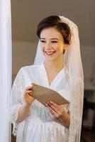 el novia en un seda traje con un velo poses en su habitación. Mañana de el novia. preparación. Boda fotografía foto