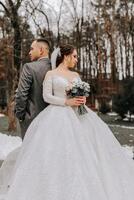 The groom comes up behind the bride and embraces her. Sincere emotions. A walk in the forest. Winter wedding photo