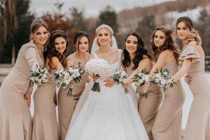 The bride and her bridesmaids pose holding bouquets and looking at the bride. Winter wedding photo