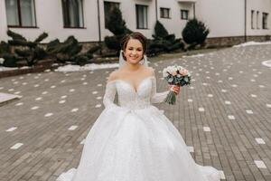 The bride in a white dress with a train and a long veil poses in nature, holding a bouquet. Walk. Winter wedding in nature. photo