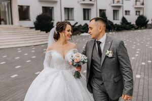 A bride in a white dress with a train and a groom in a suit pose on the steps of a building. Wedding photo session in nature