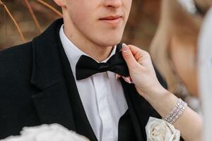 Cropped wedding portrait of the groom. The bride fixes the groom's bow tie. A man in a black suit. Winter wedding photo