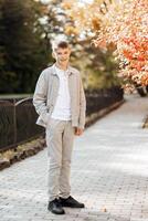 Vertical close-up portrait of a teenager in casual clothes. Happy smiling teenager in autumn park in sunlight. A beautiful child looks at the camera in nature. photo