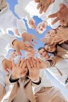 A large group of smiling young people standing, hugging, looking at the camera and stretching their arms down. Group of cheerful teenage people in a circle looking down. Low viewing angle. Copy space. photo