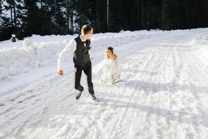 The bride and groom ride a sleigh in the winter in the snowy mountains. Winter wedding outside in the forest. The winter holidays. Happy couple sledding in snowy winter weather photo