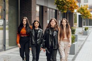 Group of smiling and happy teenage friends wearing casual clothes spending time together, posing and talking with each other near college building on autumn day. photo