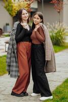 Vertical photo of two teenage friends dressed in casual clothes standing next to each other against a background of nature. Best school friends are ready to overcome anything to achieve the goal.