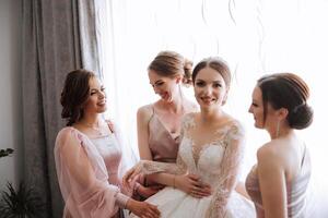 Friends rejoice with the bride in the morning. They take pictures, smile, help the bride fasten her dress. photo