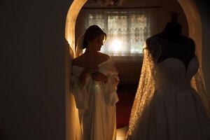 un hermosa morena novia con un tiara en su pelo es consiguiendo Listo para el Boda en un hermosa túnica en tocador estilo. de cerca Boda retrato, foto. foto