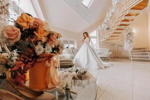 Beautiful bride in a luxurious wedding dress with a fashionable wedding hairstyle, professional make-up. Young beautiful bride in a room with a beautiful interior from the morning. High quality photo. photo