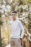 Close-up vertical portrait of a teenager in a white sweater and brown pants. Happy smiling teenager in summer park in sunlight. A beautiful child is looking at the camera in the clearing. photo