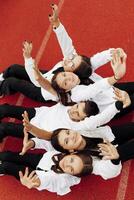 Happy friends lying together in a circle looking at the camera, holding hands and smiling while lying on a red wall... Friendship, lifestyle, togetherness, business and teamwork concepts. photo