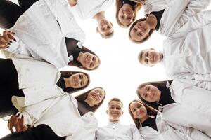 Large group of smiling young people standing, hugging, looking at camera. Group of cheerful teenage people in a circle looking down. Low viewing angle. Copy space. photo