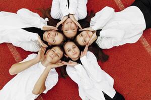 Happy friends lying together in a circle looking at the camera, holding hands and smiling while lying on a red wall... Friendship, lifestyle, togetherness, business and teamwork concepts. photo