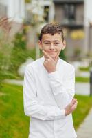 Vertical close-up portrait of a teenager in casual clothes. Happy smiling teenager in autumn park in sunlight. A beautiful child looks at the camera in nature. photo