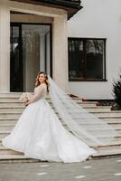 Beautiful bride with a wedding bouquet of flowers, attractive woman in a wedding dress with a long veil. Happy bride woman. Bride with wedding makeup and hairdo. Winter wedding photo