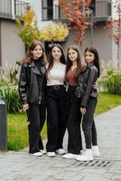 Group of smiling and happy teenage friends wearing casual clothes spending time together, posing and talking with each other near college building on autumn day. photo