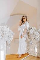 Morning of the bride before the wedding. A beautiful young woman with a veil and a beautiful hairstyle in a white robe in a room with a wonderful interior. Natural beauty and professional makeup. photo