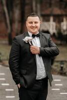 portrait of a handsome and manly groom in a black suit with a tie. Groom in nature in the winter season. photo