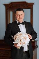 Stylish portrait of the groom with a bouquet of flowers. A man is preparing for a wedding ceremony in the morning. Groom's morning. Preparation for the groom's morning. Young and handsome groom. photo