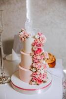 A large luxurious multi-tiered wedding cake is decorated with fresh pink rose flowers in the banquet hall. Wedding dessert under the evening light. Wedding decor. photo