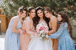 Group portrait of the bride and bridesmaids. A bride in a wedding dress and bridesmaids in beautiful dresses hold the bride's bouquet on the wedding day. photo