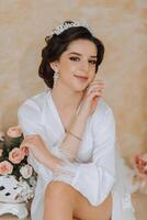 Morning of the bride before the wedding. A beautiful young woman with a veil and a beautiful hairstyle in a white robe in a room with a wonderful interior. Natural beauty and professional makeup. photo