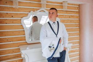 A stylish portrait of the groom preparing for the wedding ceremony in the morning. Groom's morning. Preparation for the groom's morning. The groom puts on a jacket. The confident look of a mature man. photo