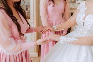 A friend helps the bride fasten her dress. A woman helps her friend fasten the buttons on the back of her wedding dress. The morning of the bride, the creation of a family, an important event. photo