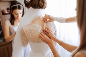 Morning of the bride. The bride's maid of honor helps the bride lace up her dress, fasten buttons on the dress or sleeves. Girlfriends help the bride fasten her dress photo