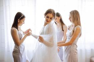 Morning of the bride. The bride's maid of honor helps the bride lace up her dress, fasten buttons on the dress or sleeves. Girlfriends help the bride fasten her dress photo