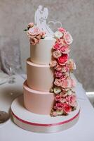 A large luxurious multi-tiered wedding cake is decorated with fresh pink rose flowers in the banquet hall. Wedding dessert under the evening light. Wedding decor. photo