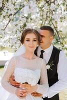 Wedding. Love and couple in garden for wedding. Celebration of ceremony and commitment. Save the date. Trust. The bride and groom embrace. The groom embraces the bride under a spring flowering tree. photo