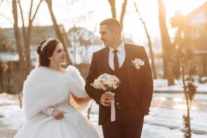 Winter wedding. Happy couple walking in wedding clothes hugging and smiling in a winter park covered with snow on their wedding day. Winter love story of a beautiful couple in snowy winter weather photo