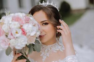 morena novia en fuera del hombro cordón blanco vestir y tiara posando con un ramo de flores de blanco y rosado flores hermosa pelo y constituir. primavera Boda foto