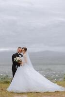 The bride and groom stand face to face with green hills in the background. A beautiful photo session of the bride and groom in the mountains. Free space.