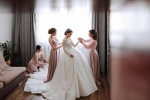 Friends rejoice with the bride in the morning. They take pictures, smile, help the bride fasten her dress. photo