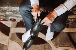 un elegante hombre usa negro cuero formal zapatos. atadura zapatos. negocio hombre atadura cordones de los zapatos en el piso. arriba cerca el novio es preparando para el boda. foto