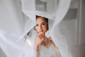 A luxurious bride with a beautiful hairstyle and a gorgeous dress is getting ready for the wedding ceremony in the morning. Morning photo of the bride at home or in a hotel room. Professional makeup.