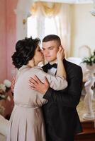 mother helps her adult son prepare for the wedding ceremony. An emotional and touching moment at a wedding. A mother hugs her son photo