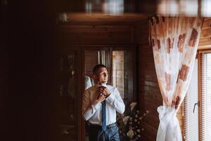 un elegante novio es atadura su atar, preparando para el Boda ceremonia. del novio Mañana. un empresario usa un atar. el novio es consiguiendo Listo en el Mañana antes de el Boda ceremonia. foto