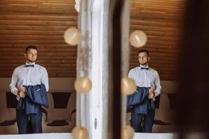 elegante y lujoso hombre participación su chaqueta antes de vendaje en hotel habitación con reflexión en espejo. foto