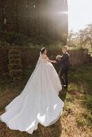 Portrait of young bride and groom walking on green grass during sunset after wedding ceremony, front view. Happy wedding couple, copy space photo