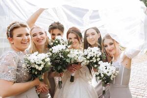 Group portrait of the bride and bridesmaids. A bride in a wedding dress and bridesmaids in silver dresses hold stylish bouquets on their wedding day. photo