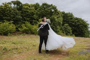 The bride in the arms of the groom. The groom is holding his bride in his arms and circling against the background of a beautiful park. photo