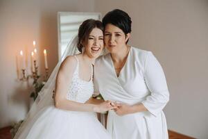 A beautiful and happy mother and her daughter, the bride, are standing next to each other. The best day for parents. Tender moments at the wedding. photo