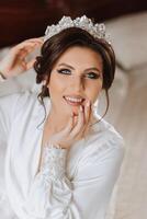 A beautiful brunette bride with a tiara in her hair is getting ready for the wedding in a beautiful robe in boudoir style. Close-up wedding portrait, photo. photo