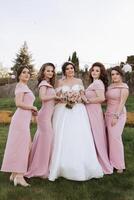 grupo retrato de el novia y damas de honor novia en un Boda vestir y damas de honor en rosado o polvo vestidos y participación elegante ramos de flores en el Boda día. foto