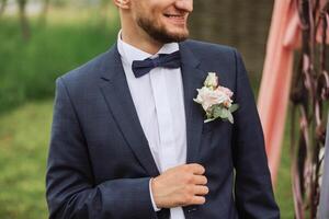 The groom in a black tuxedo and bowtie adjusts his jacket. Wedding. Details photo